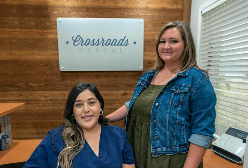 Front office Team Smiling in front of Crossroads Dental sign